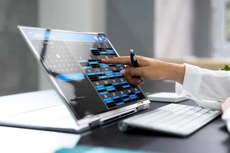 A person using a stylus on a digital calendar on a laptop screen.