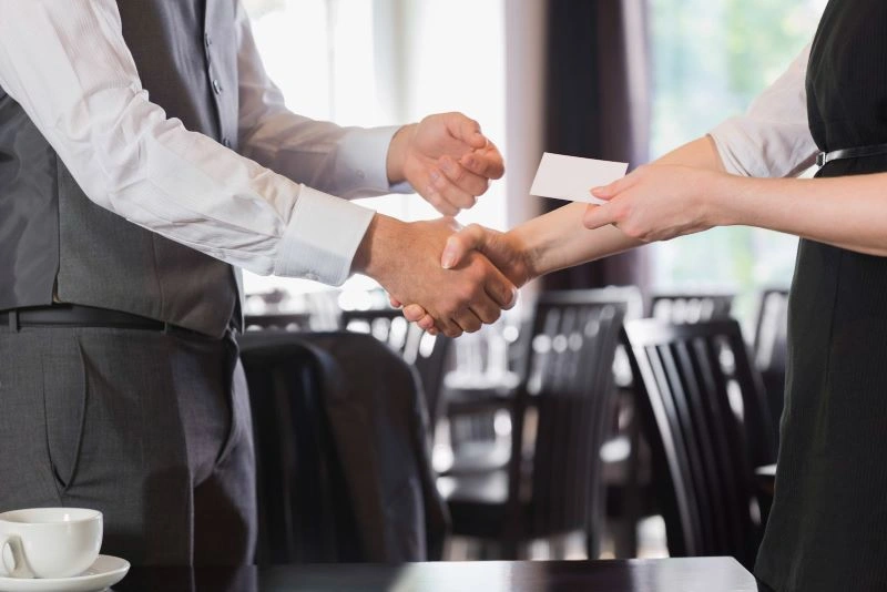A man and woman shaking hands while exchanging business cards.