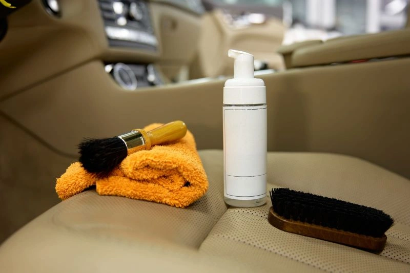 A microfiber towel, cleaning brush, and foam dispenser on a car seat.